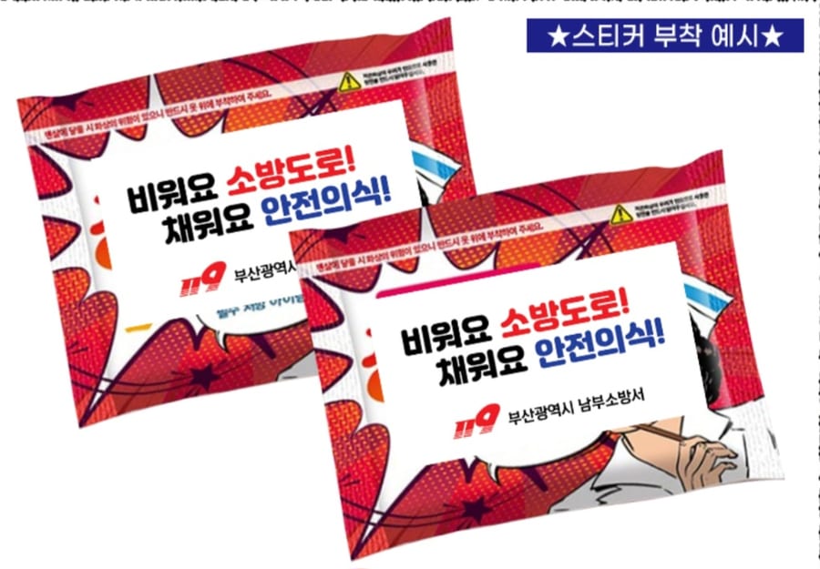 빨간 미니 핫팩 봉투 두 개에 흰 바탕 홍보 스티커를 붙인 예시 — 「비워요 소방도로! 채워요 안전의식!」 문구와 부산광역시 남부소방서 로고