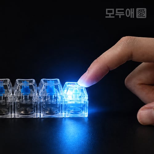 손가락으로 누른 투명 키캡 키링에서 파란 LED 불빛이 켜진 모습