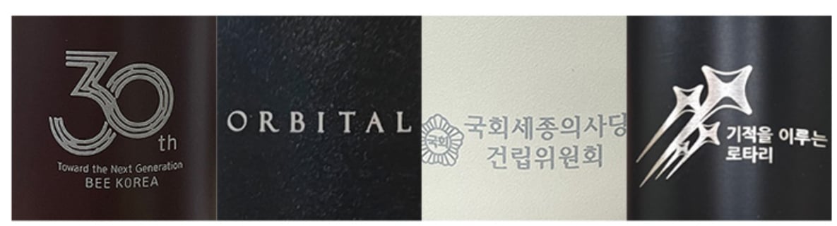 레이저 각인한 로고 4종 — 짙은 색 코팅 텀블러와 밝은 색 제품에 코팅을 깎아 금속색 로고를 낸 모습. 가는 선과 작은 글자도 또렷하게 남습니다